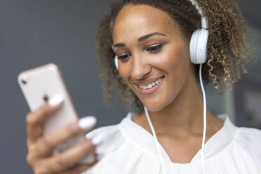Porträt einer lächelnden jungen Frau mit Smartphone und weißen Kopfhörern - MOEF02357