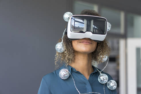 Lächelnde junge Frau mit Lichterkette unter Verwendung einer Virtual-Reality-Brille - MOEF02379
