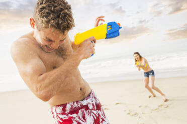 Kaukasisches Paar spielt mit Spritzpistolen am Strand - BLEF09095