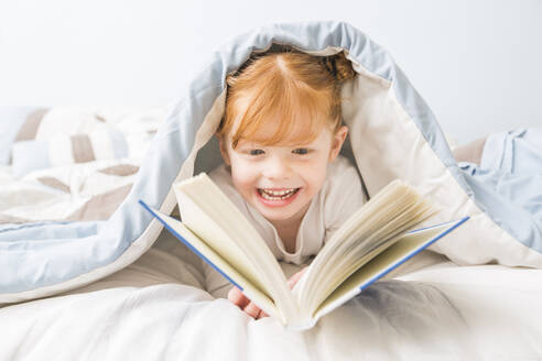 Caucasian girl reading book in bed - BLEF09118