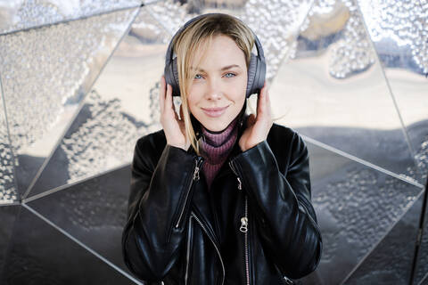 Porträt einer lächelnden jungen Frau, die mit drahtlosen Kopfhörern Musik hört, lizenzfreies Stockfoto