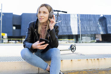 Porträt einer jungen Frau, die mit Smartphone und Kopfhörern Musik hört, Barcelona, Spanien - GIOF06612