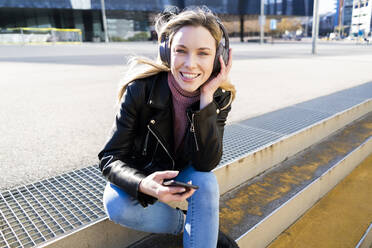 Porträt einer jungen Frau, die mit Smartphone und Kopfhörern Musik hört, Barcelona, Spanien - GIOF06615