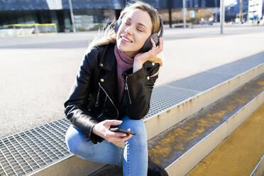 Porträt einer jungen Frau, die mit Smartphone und Kopfhörern Musik hört, Barcelona, Spanien - GIOF06616