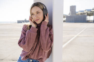 Porträt einer lächelnden jungen Frau, die mit drahtlosen Kopfhörern Musik hört, Barcelona, Spanien - GIOF06623