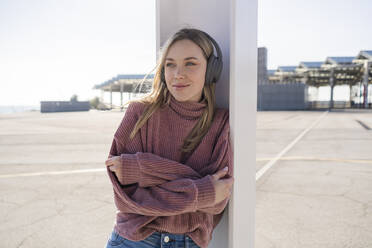 Porträt einer lächelnden jungen Frau, die mit drahtlosen Kopfhörern Musik hört, Barcelona, Spanien - GIOF06624