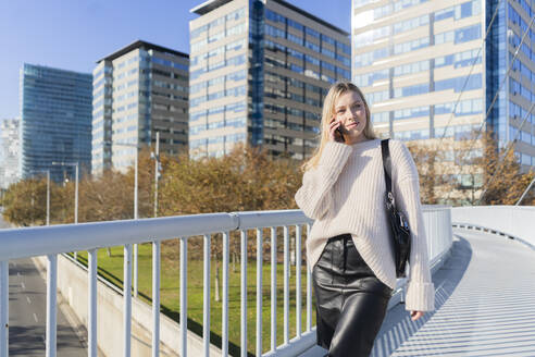 Porträt einer blonden jungen Frau am Telefon auf einer Fußgängerbrücke - GIOF06658