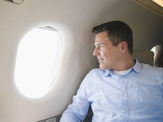 Kaukasischer Geschäftsmann schaut aus dem Flugzeugfenster - BLEF09212