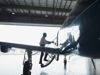 Caucasian pilot boarding airplane in hangar - BLEF09229