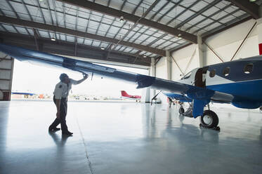 Caucasian pilot examining airplane in hangar - BLEF09230