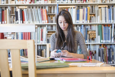 Studentin hört in der Bibliothek Kopfhörer - BLEF09234