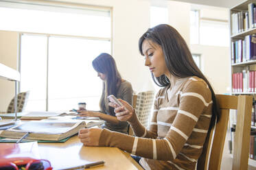 Student benutzt Handy am Schreibtisch in der Bibliothek - BLEF09235