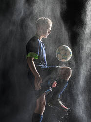 Caucasian soccer player kicking ball in rain - BLEF09285