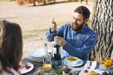 Caucasian man opening wine bottle at outdoor table - BLEF09307