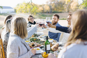 Freunde stoßen am Tisch im Freien mit Wein an - BLEF09313