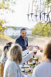 Freunde stoßen am Tisch im Freien mit Wein an - BLEF09318