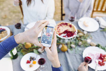 Kaukasischer Mann fotografiert Essen an einem Tisch im Freien - BLEF09324