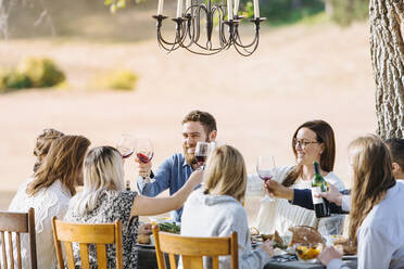 Freunde stoßen am Tisch im Freien mit Wein an - BLEF09334