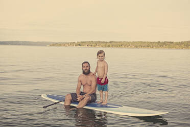 Kaukasischer Vater und Sohn auf einem Paddelbrett im See - BLEF09428