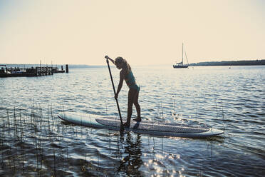 Kaukasisches Mädchen steht auf einem Paddleboard im See - BLEF09430