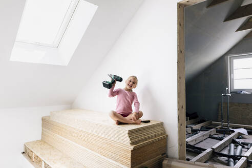 Portrait of a happy girl with electric drill in a home to be renovated - KMKF00992