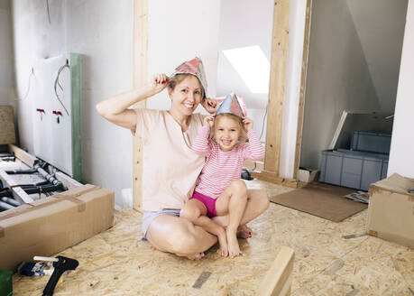 Happy mother and daughter wearing paper hats in a home to be renovated - KMKF00997