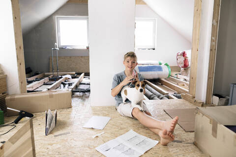 Porträt eines lächelnden Jungen mit Hund in einem zu renovierenden Haus, lizenzfreies Stockfoto