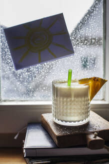 Ein Glas Pina Colada steht vor einem mit Regentropfen bedeckten Fenster - SBDF03969