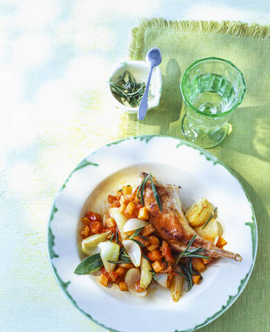 Draufsicht auf eine Kaninchenkeule mit Zwiebeln und Gemüse auf einem Tisch im Freien, lizenzfreies Stockfoto