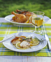 Roasted chicken in lemon sauce and glass of white wine on garden table - PPXF00206