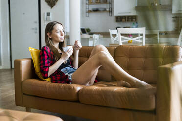 Entspannte junge Frau isst Müsli im Wohnzimmer zu Hause - GIOF06665