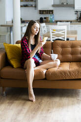 Junge Frau benutzt Handy auf einer Couch zu Hause - GIOF06670