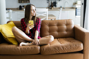 Junge Frau mit Mobiltelefon auf einer Couch zu Hause - GIOF06671