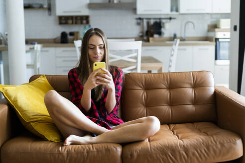 Junge Frau benutzt Handy auf einer Couch zu Hause - GIOF06672