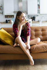 Glückliche junge Frau, die auf einer Couch zu Hause ein Handy benutzt - GIOF06677