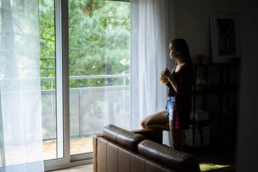 Junge Frau schaut zu Hause aus dem Fenster - GIOF06683