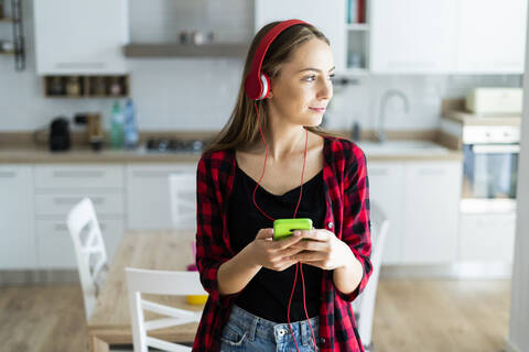 Junge Frau mit Mobiltelefon und Kopfhörern zu Hause, lizenzfreies Stockfoto