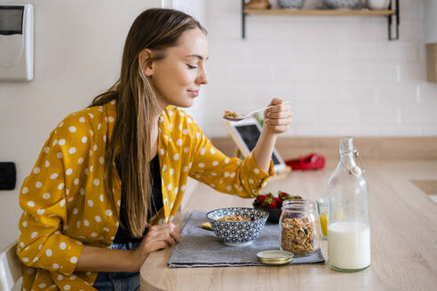 Junge Frau genießt das Frühstück in der Küche zu Hause - GIOF06700