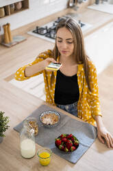 Junge Frau, die mit ihrem Handy ein Foto von ihrem Frühstück zu Hause macht - GIOF06704