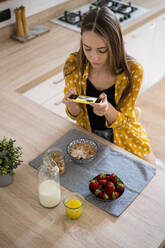 Junge Frau, die mit ihrem Handy ein Foto von ihrem Frühstück zu Hause macht - GIOF06705