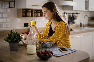 Junge Frau benutzt ein Tablet und frühstückt in der Küche zu Hause - GIOF06707