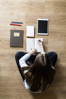 Top view of young woman sitting on the floor at home taking notes - GIOF06708
