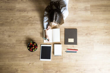 Top view of young woman lying on the floor at home taking notes - GIOF06709