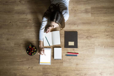 Top view of young woman lying on the floor at home using a tablet - GIOF06710