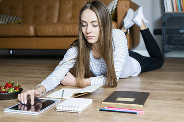 Young woman lying on the floor at home using a tablet - GIOF06711