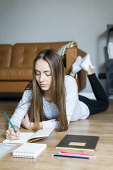 Young woman lying on the floor at home taking notes - GIOF06712