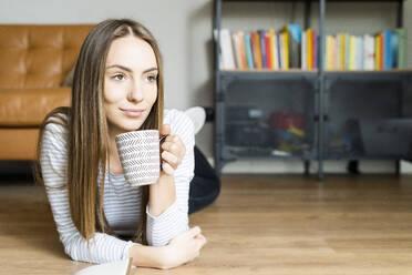 Relaxed young woman lying on the floor at home drinking coffee - GIOF06715