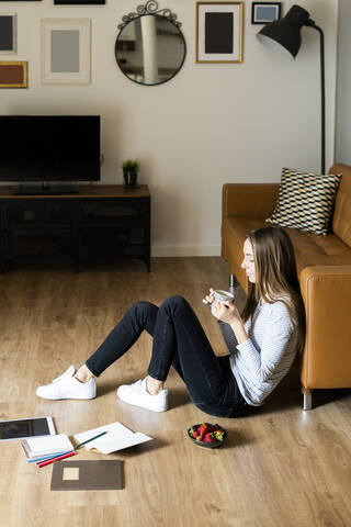 Entspannte junge Frau, die zu Hause auf dem Boden sitzt und Kaffee trinkt, lizenzfreies Stockfoto