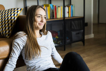 Smiling relaxed young woman sitting on the floor at home - GIOF06718