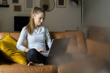 Young woman using laptop on couch at home - GIOF06719